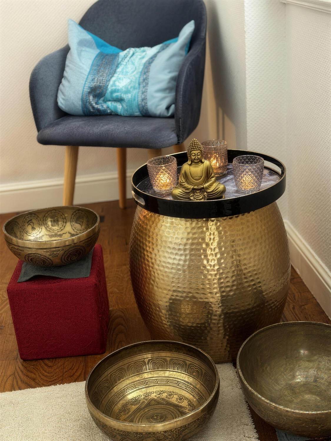 Messing-Klangschalen, Buddha-Figur und ein goldener Beistelltisch neben einem Sessel in der Praxis